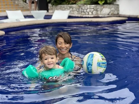 Zoe smiling in a green pool float with a family member