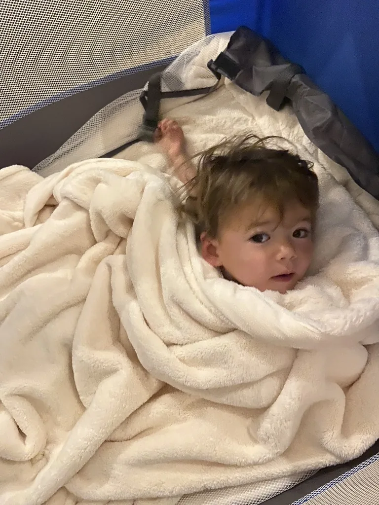 Zoe tucked into a travel crib with a white blanket