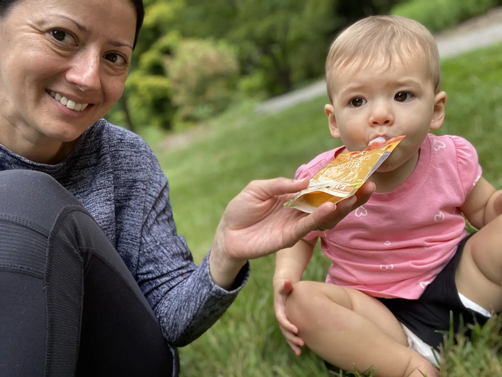 Marie smiling while Zoe eats from a pouch outside in Asheville