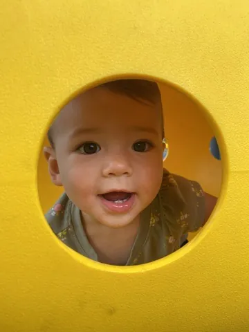 Zoe peeking through a yellow playground tunnel