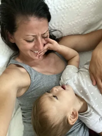 Marie laughing while Zoe reaches toward her face in bed