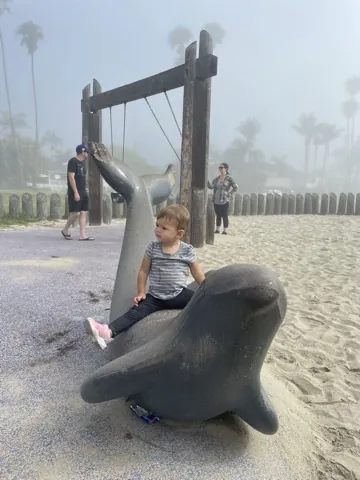 Zoe sitting on a playground sea-creature sculpture in beach fog