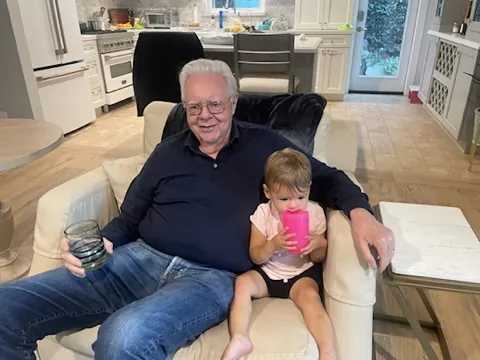 Zoe sitting in an armchair beside her grandfather with a pink cup