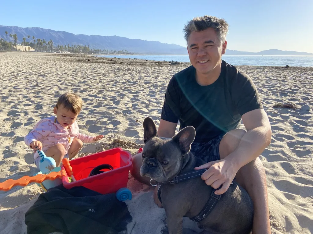 Andrew sitting with Zoe and Francis on the sand at East Beach