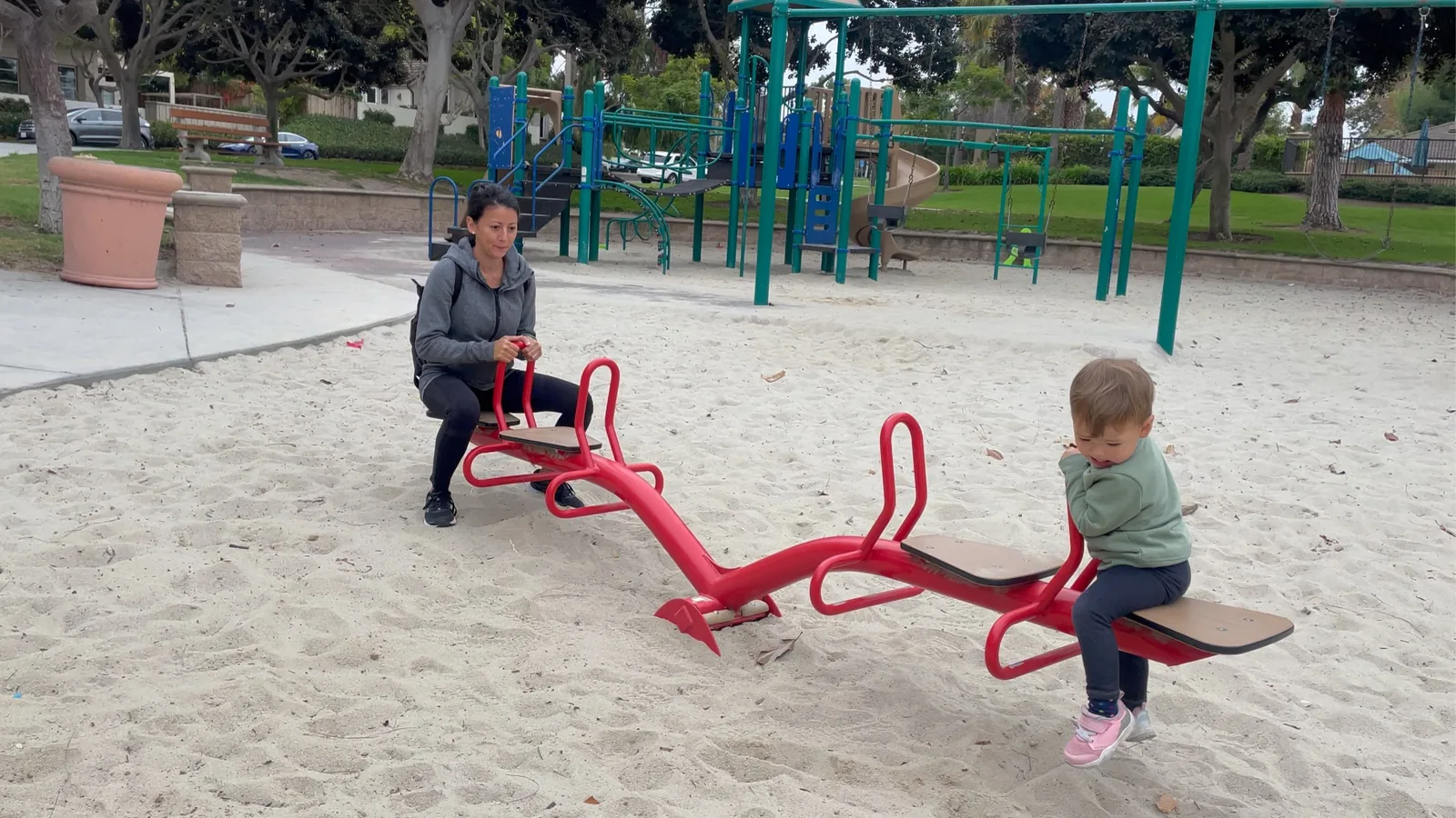 Marie and Zoe on a red seesaw at a sandy playground