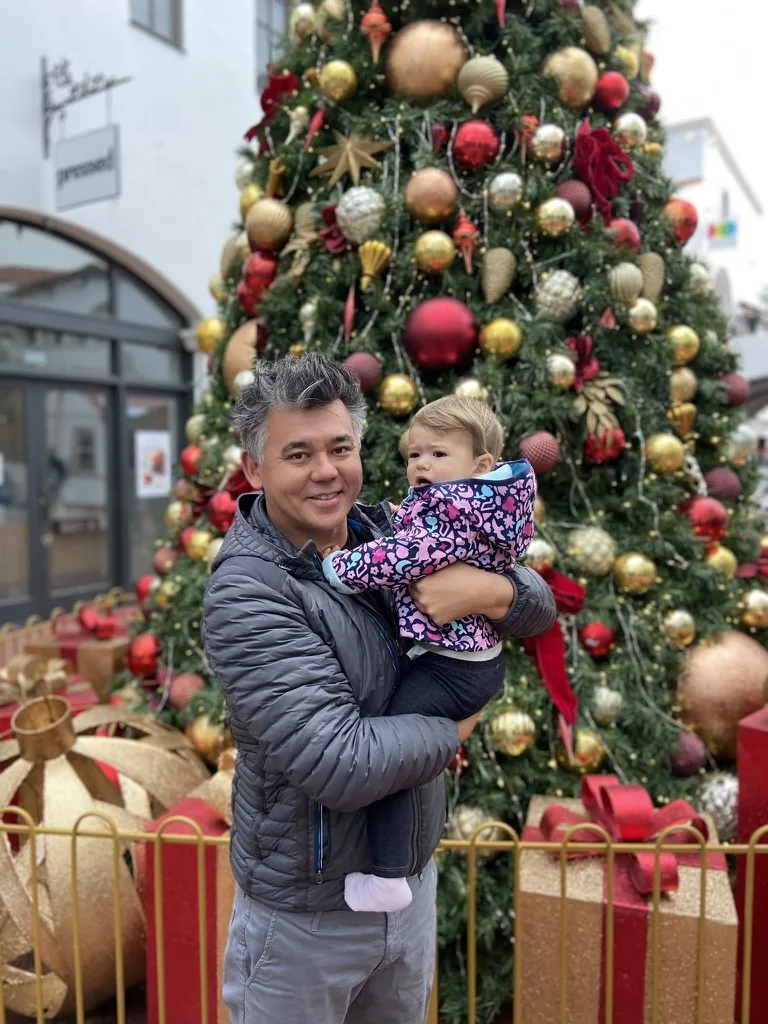 Andrew holding Zoe in front of a decorated Christmas tree