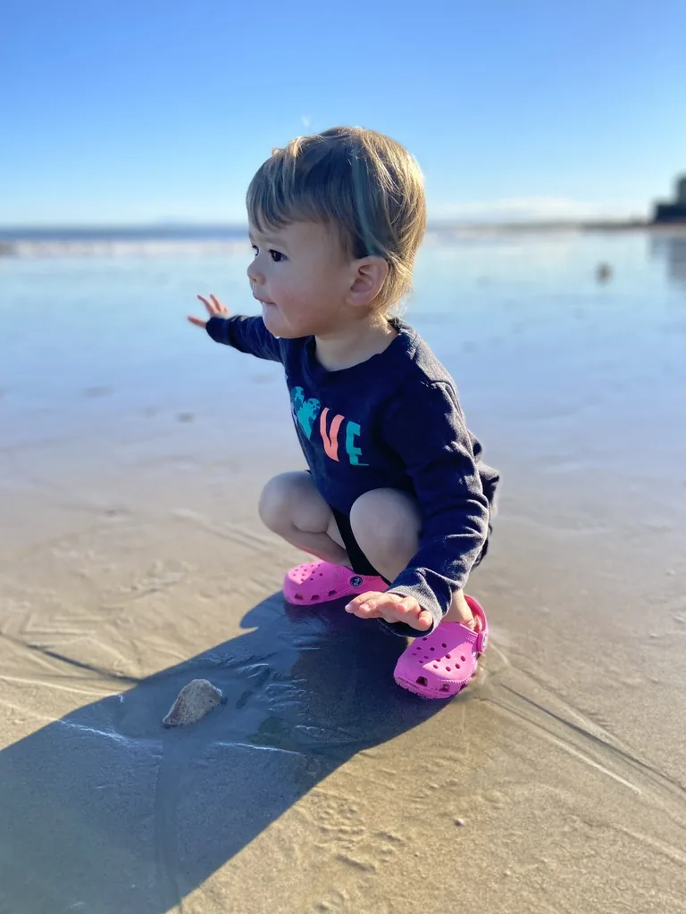 Zoe crouching on wet sand at the beach
