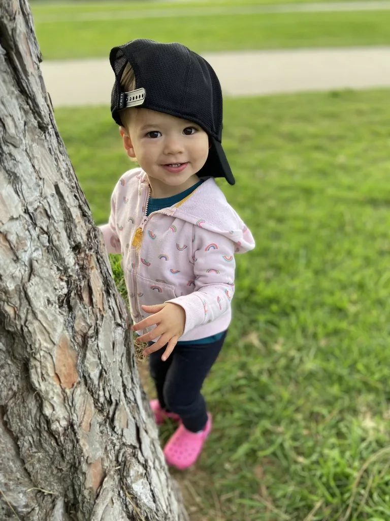 Zoe smiling beside a tree while wearing a backwards black cap