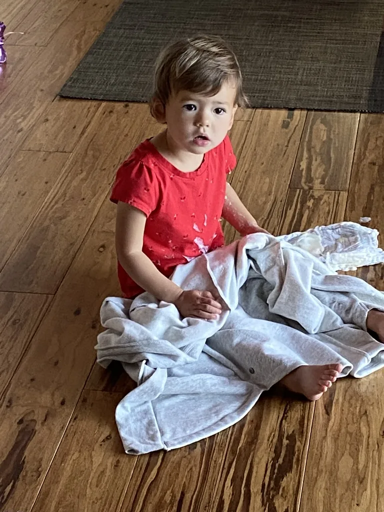 Zoe sitting on the floor in a red shirt with folded clothes nearby