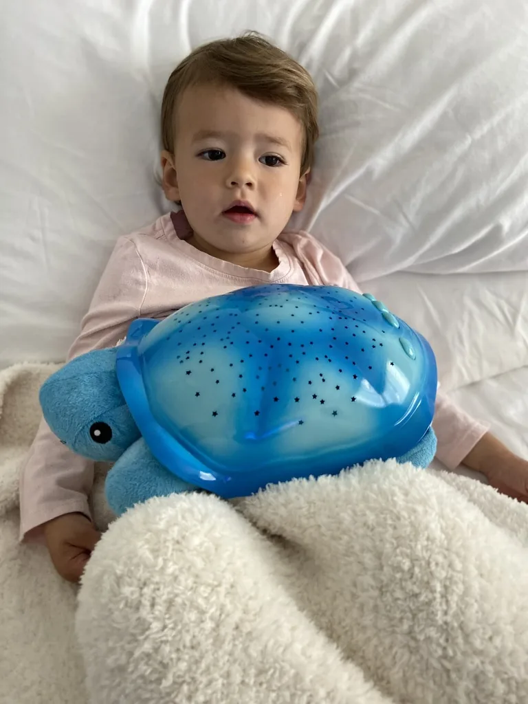 Zoe holding a blue turtle night light under a blanket