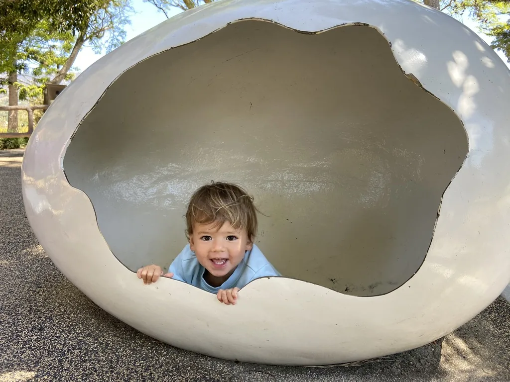 Zoe peeking out from a white egg-shaped playground structure