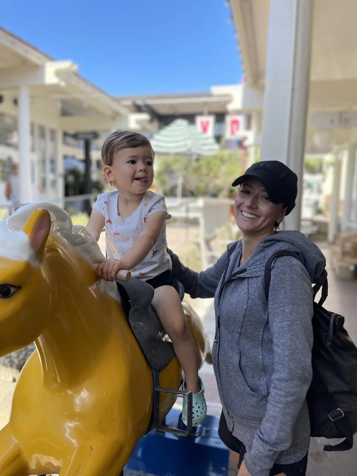 Marie smiling beside Zoe on a yellow kiddie ride