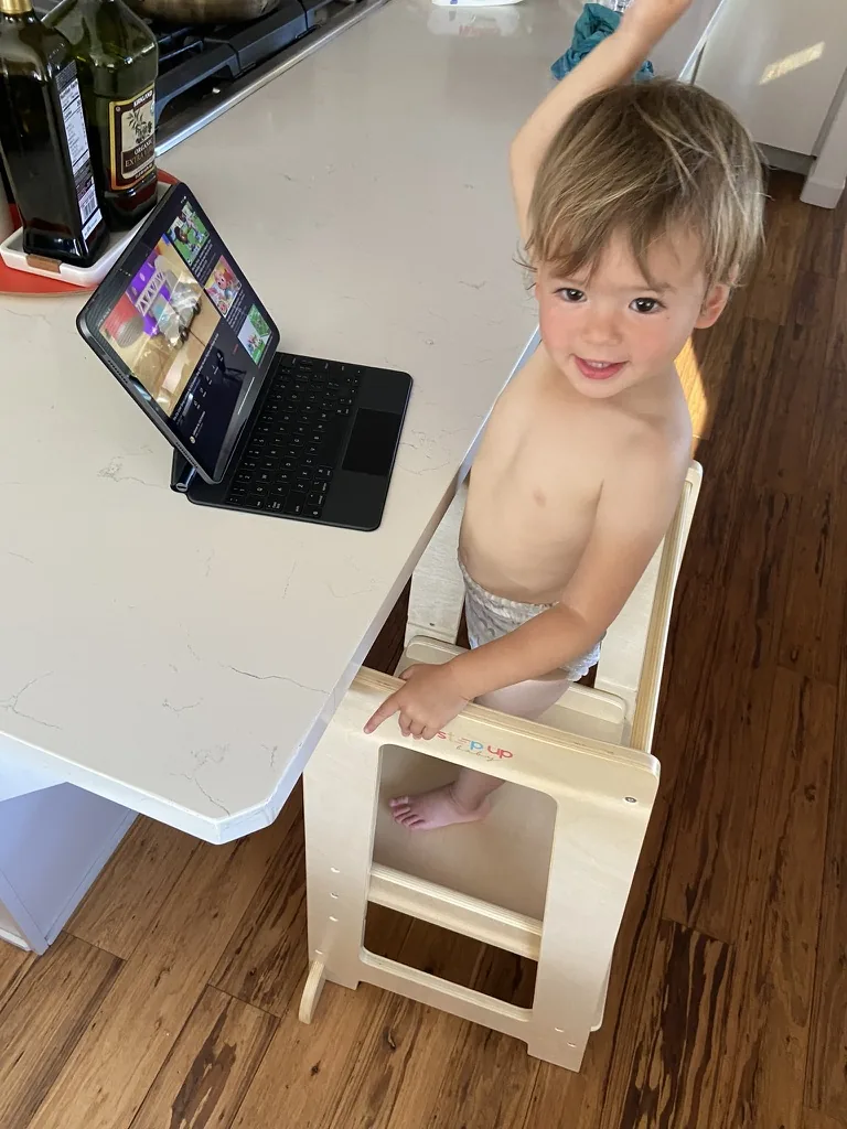 Zoe standing in a kitchen learning tower beside a tablet