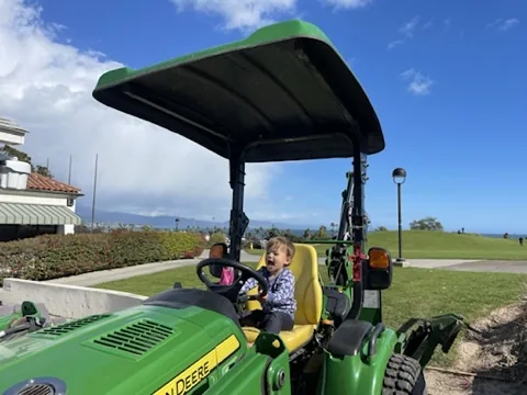 Zoe sitting on a green John Deere tractor with ocean in the distance