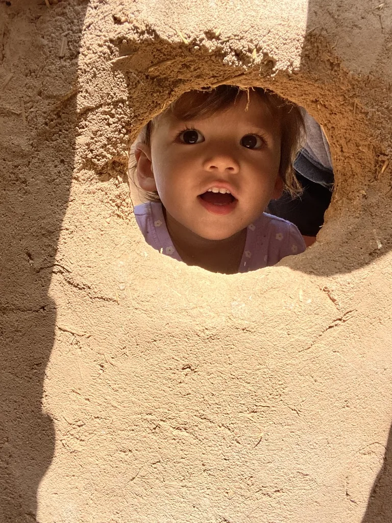 Zoe looking through a round mud play window