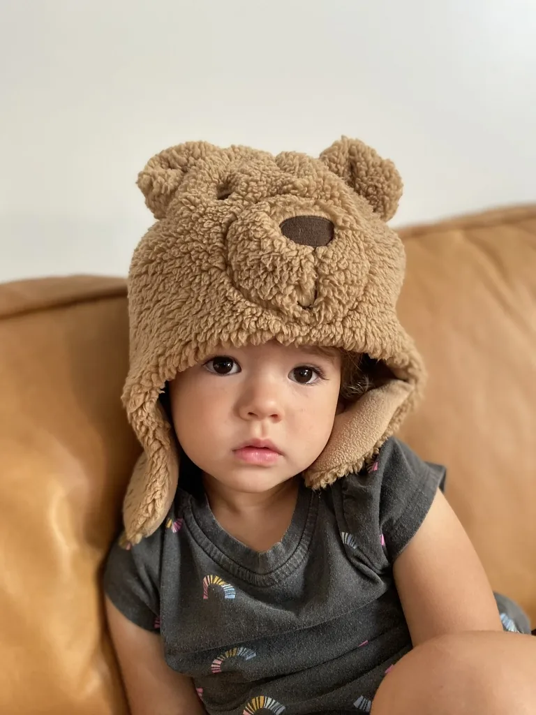 Zoe wearing a plush bear hat on a couch