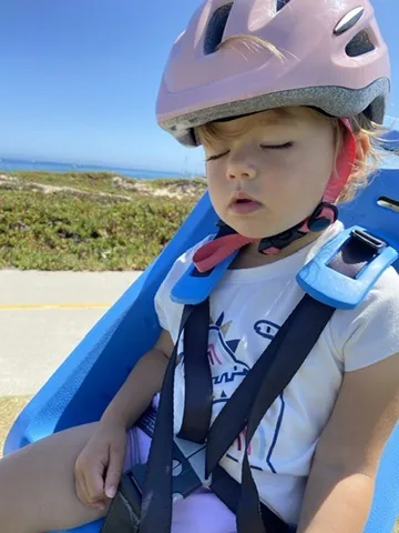 Zoe sleeping in a blue bike trailer with a helmet on