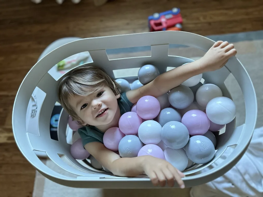 Zoe smiling from inside a laundry basket filled with pastel balls
