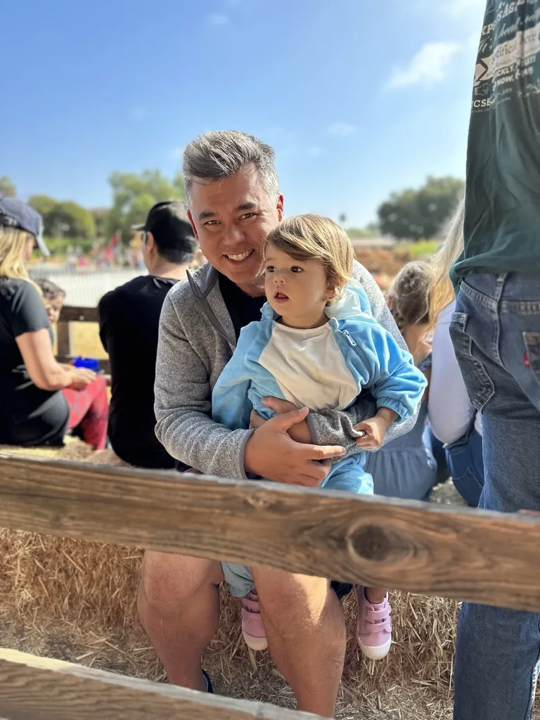 Andrew holding Zoe while sitting on hay bales at a pumpkin patch