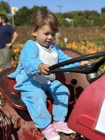 Zoe sitting on a red tractor at a pumpkin patch