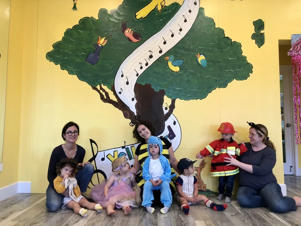 Zoe in a blue shark costume sitting with other children in costume at music class