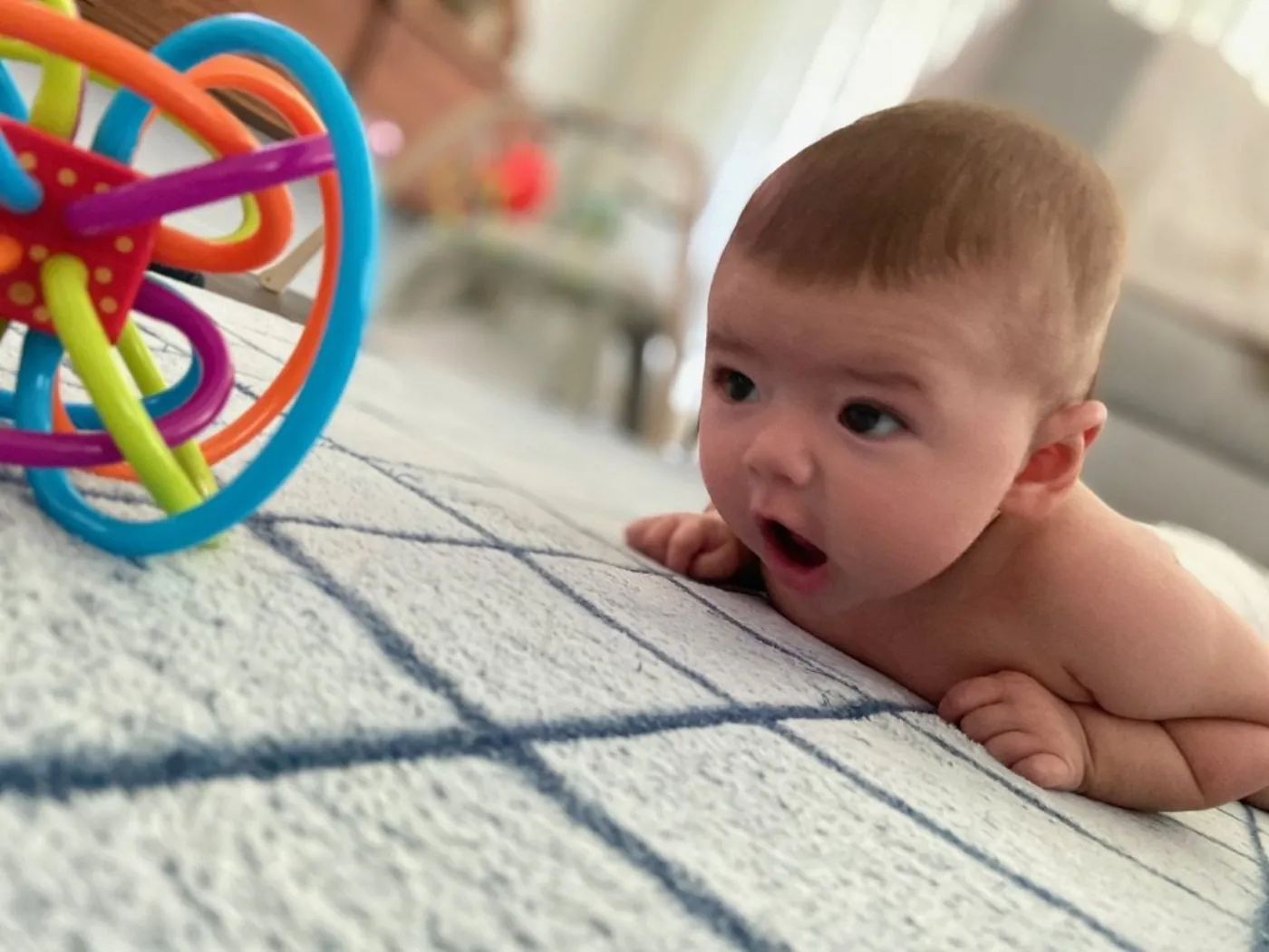 Zoe doing tummy time and looking at a colorful rattle toy
