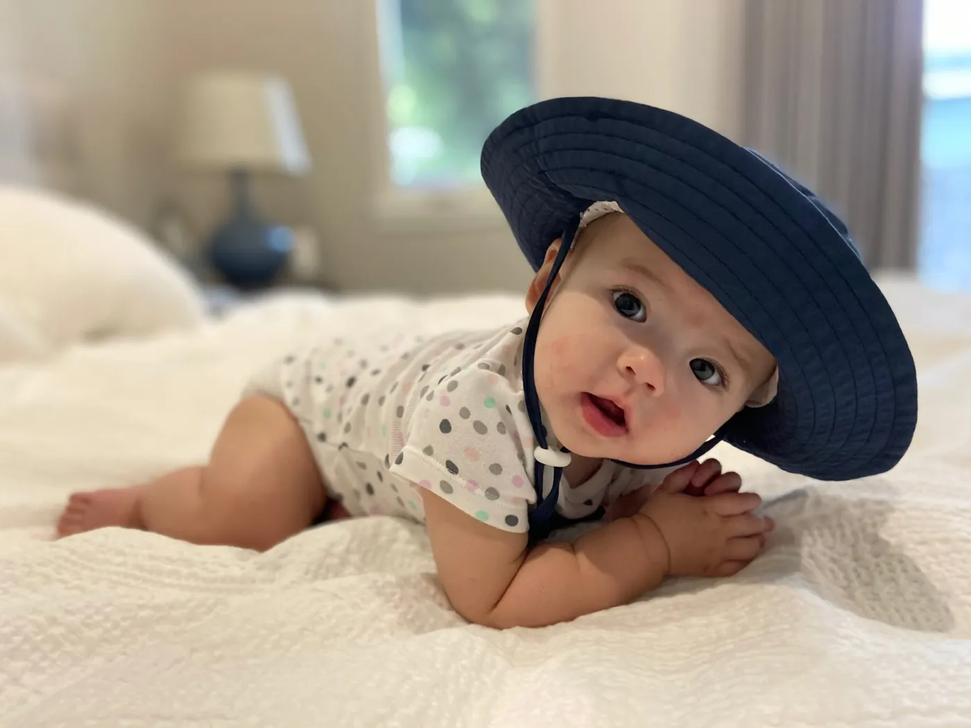Zoe wearing a blue sun hat on a white bed