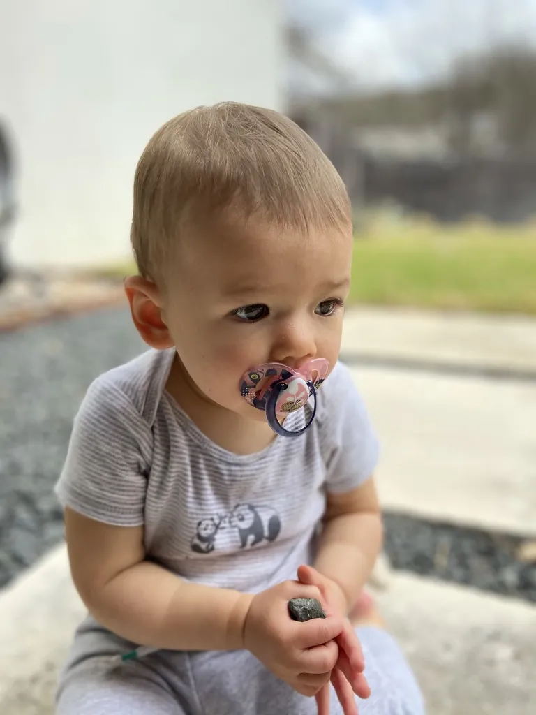 Zoe sitting on a patio with a pacifier while holding a small rock